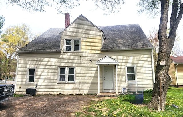 cape cod house featuring roof with shingles, a chimney, and central AC