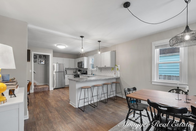 kitchen with appliances with stainless steel finishes, tasteful backsplash, white cabinetry, kitchen peninsula, and dark wood-type flooring