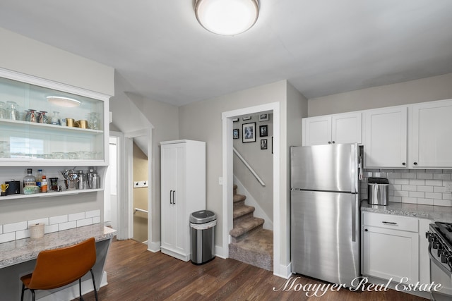 kitchen featuring dark wood-type flooring, stainless steel refrigerator, light stone countertops, gas range oven, and white cabinets