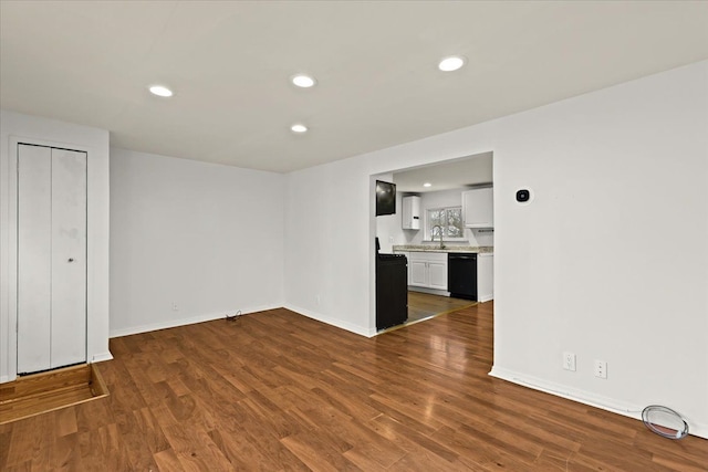 unfurnished living room featuring recessed lighting, dark wood-style flooring, a sink, and baseboards