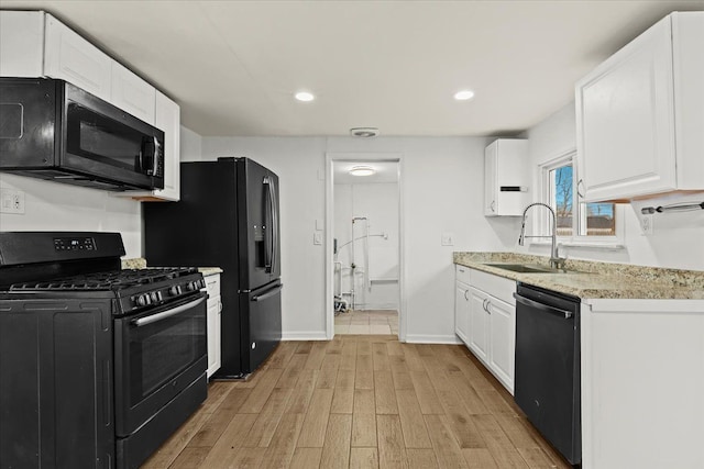 kitchen with light wood-style floors, white cabinetry, a sink, black appliances, and baseboards