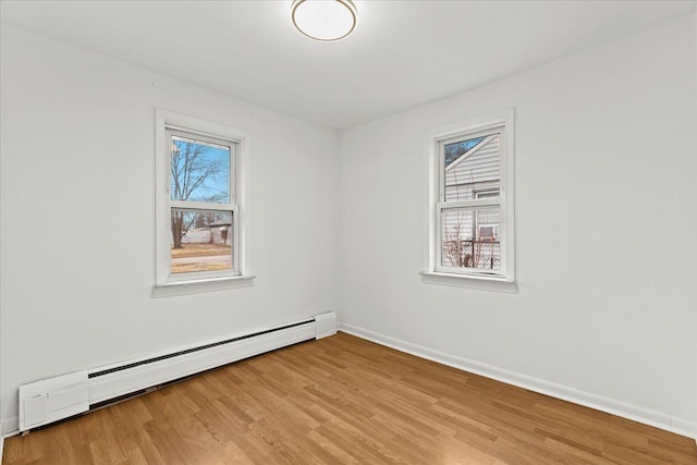 unfurnished room with light wood finished floors, baseboard heating, a wealth of natural light, and baseboards