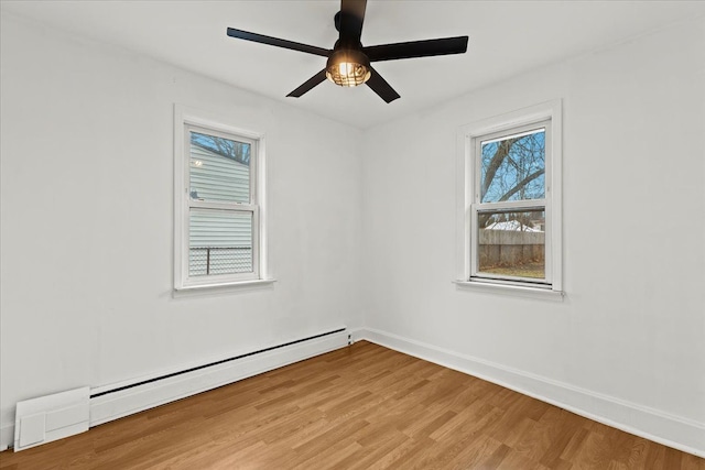 empty room featuring a baseboard heating unit, ceiling fan, light wood finished floors, and baseboards