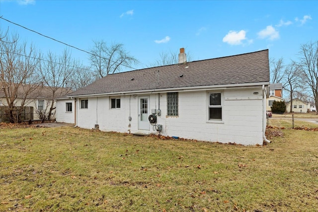 back of property with roof with shingles, a lawn, a chimney, and fence