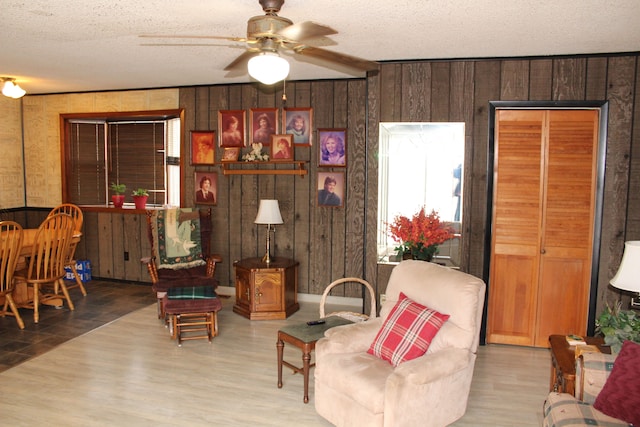 living room with hardwood / wood-style floors, wood walls, a textured ceiling, and ceiling fan