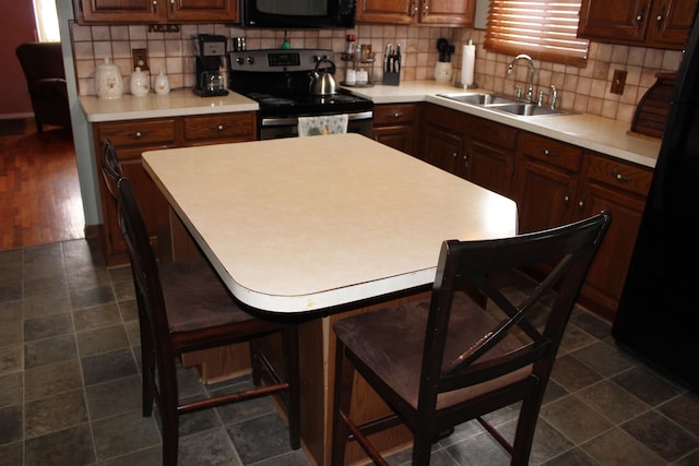 kitchen with sink, decorative backsplash, black appliances, and a kitchen bar