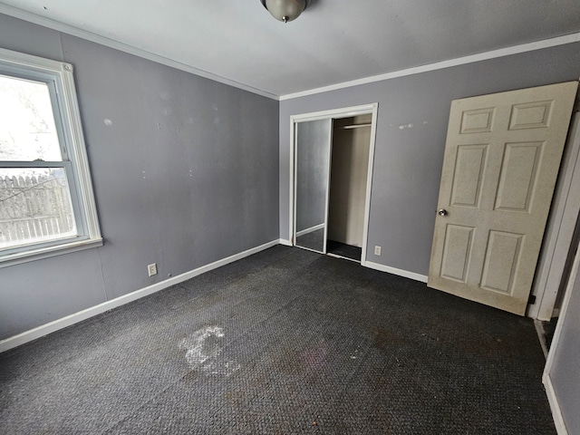 unfurnished bedroom featuring dark colored carpet, crown molding, and a closet