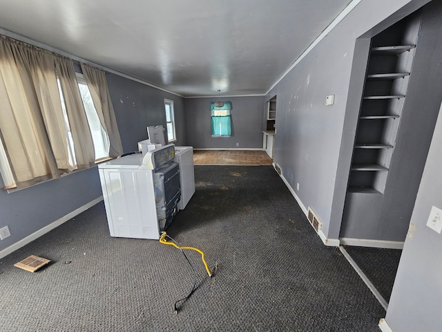 unfurnished living room featuring crown molding, washer / dryer, and dark colored carpet