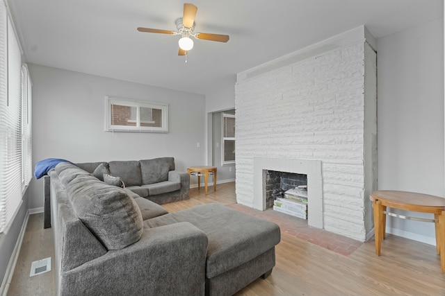 living room featuring a stone fireplace, light hardwood / wood-style flooring, and ceiling fan