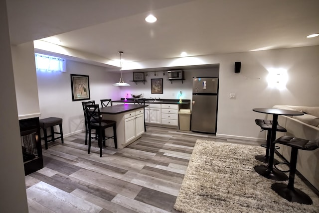 kitchen featuring a breakfast bar, stainless steel refrigerator, white cabinetry, sink, and hanging light fixtures