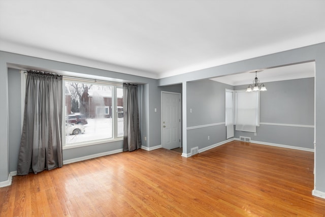 spare room with an inviting chandelier and light hardwood / wood-style floors