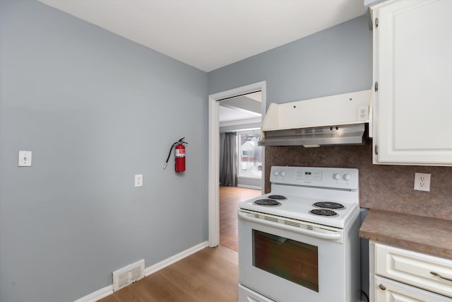 kitchen featuring white electric range, hardwood / wood-style flooring, white cabinetry, decorative backsplash, and custom exhaust hood