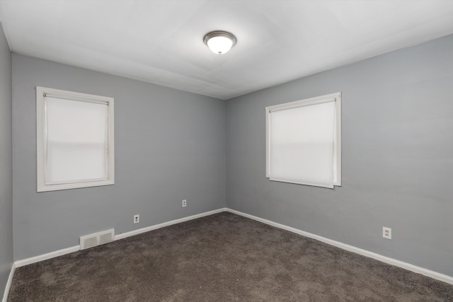 unfurnished room with a wealth of natural light and dark carpet