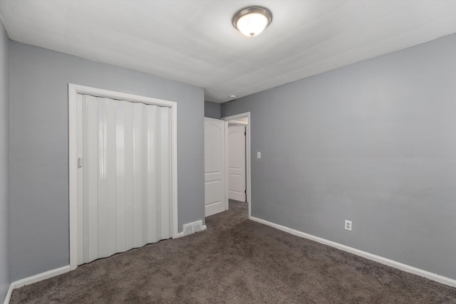 unfurnished bedroom with dark colored carpet and a closet