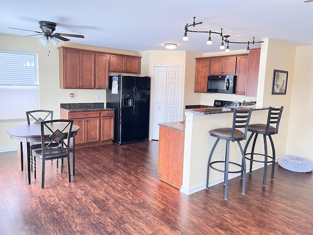 kitchen featuring dark wood-type flooring, black appliances, dark stone counters, and a breakfast bar