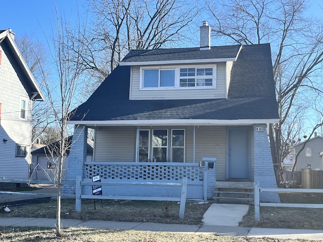 view of front of house featuring brick siding, a chimney, a shingled roof, covered porch, and fence