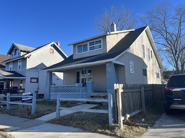 bungalow featuring covered porch, a fenced front yard, and a chimney