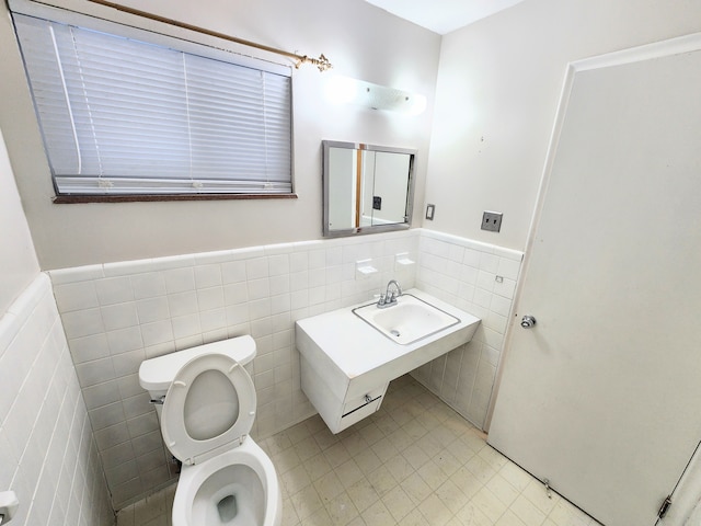 bathroom featuring a sink, a wainscoted wall, toilet, and tile walls