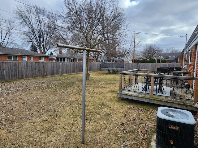 view of yard with a wooden deck, outdoor dining area, a fenced backyard, central AC, and a trampoline