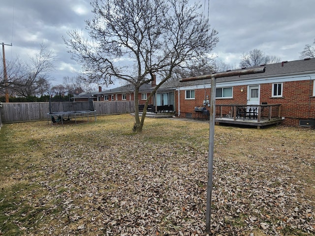 view of yard featuring a fenced backyard, a deck, and a trampoline