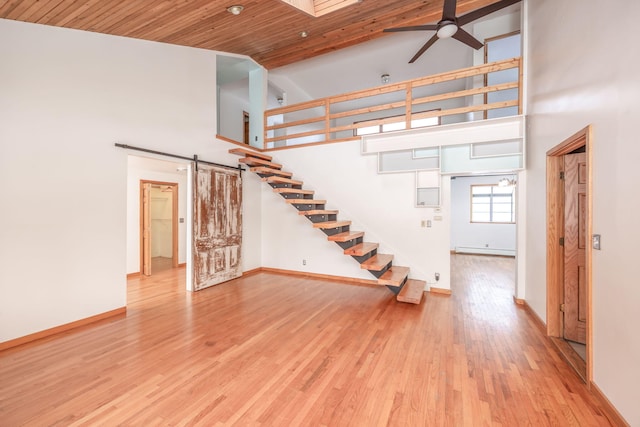 unfurnished living room featuring light hardwood / wood-style flooring, ceiling fan, a barn door, and a high ceiling