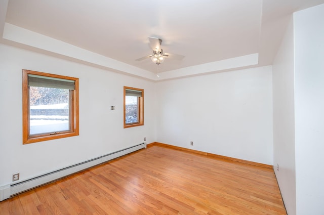 spare room with baseboard heating, light hardwood / wood-style flooring, a raised ceiling, and ceiling fan