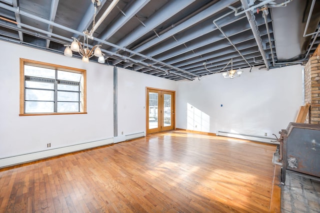 unfurnished living room featuring an inviting chandelier, baseboard heating, wood-type flooring, and french doors