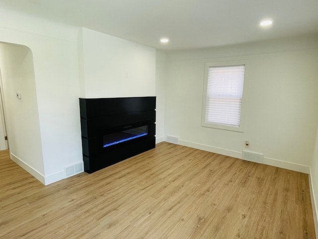 unfurnished living room featuring visible vents, a glass covered fireplace, light wood-style flooring, and baseboards