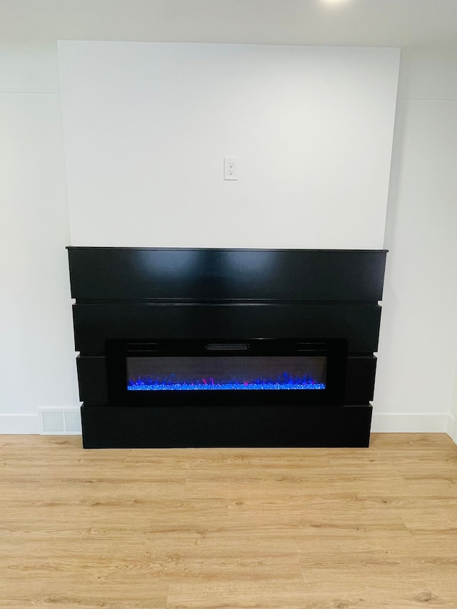 details with a glass covered fireplace, visible vents, baseboards, and wood finished floors