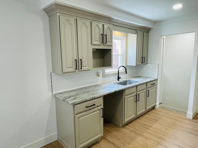 kitchen with light wood-style floors, a sink, backsplash, and baseboards