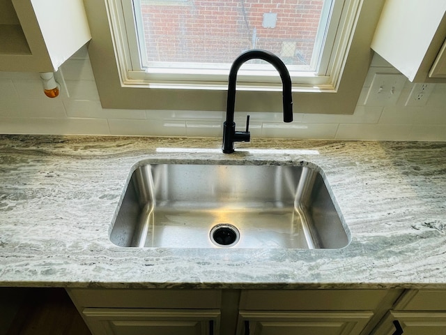 room details featuring light stone counters, cream cabinetry, a sink, and backsplash