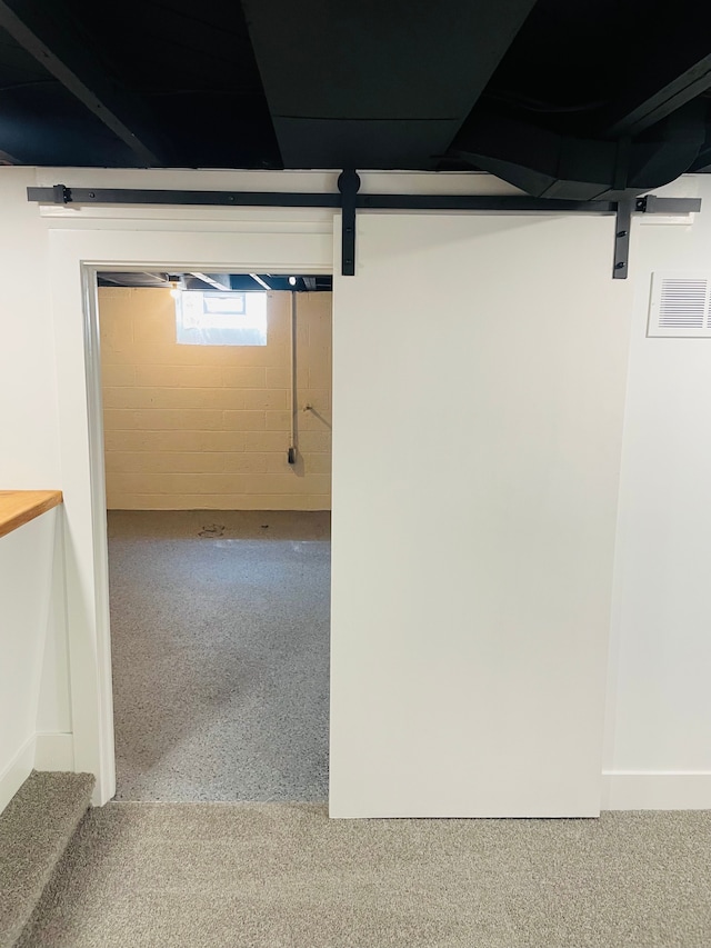 basement with concrete block wall, a barn door, and visible vents