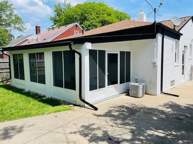 view of property exterior with a sunroom, a chimney, brick siding, and a patio