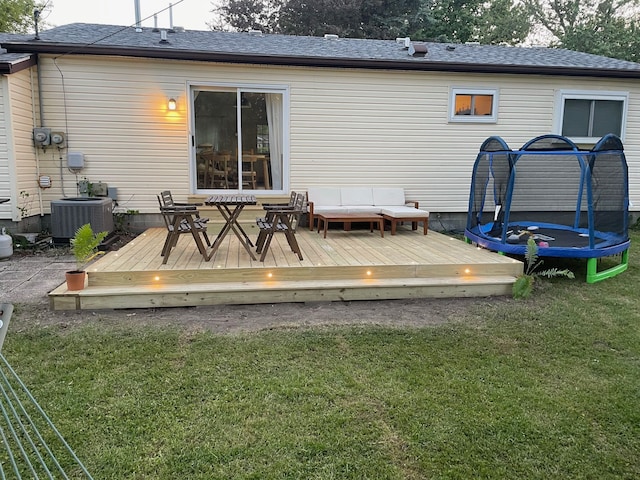 rear view of property featuring a deck, a trampoline, a yard, central AC unit, and an outdoor living space