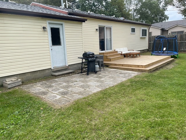 rear view of house with a trampoline, a yard, a patio, and a deck