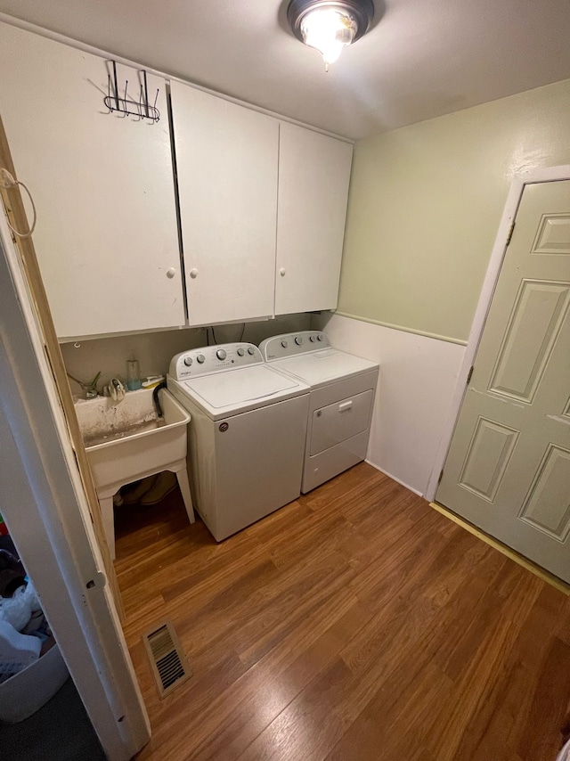 laundry room featuring separate washer and dryer, sink, hardwood / wood-style flooring, and cabinets