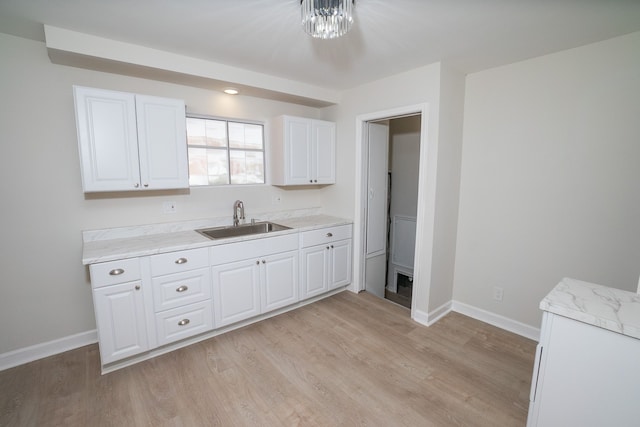 kitchen with sink, light stone counters, a notable chandelier, light hardwood / wood-style floors, and white cabinets