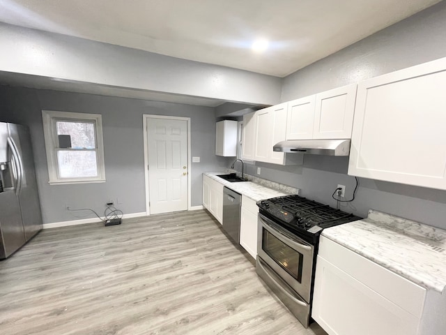 kitchen with appliances with stainless steel finishes, sink, white cabinets, and light hardwood / wood-style flooring