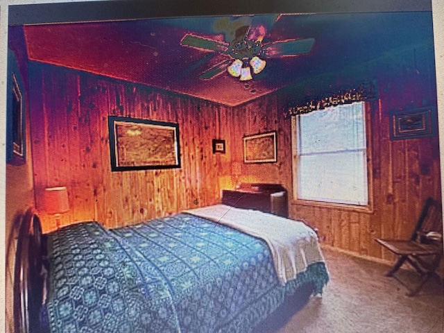 carpeted bedroom featuring ceiling fan and wood walls