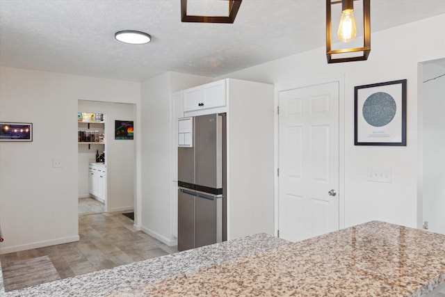 kitchen featuring stainless steel refrigerator, light stone counters, a textured ceiling, white cabinets, and decorative light fixtures