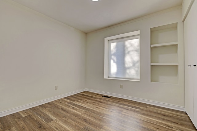 empty room with built in shelves, ornamental molding, and wood-type flooring