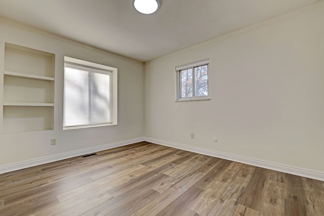 unfurnished room featuring crown molding, built in shelves, and light hardwood / wood-style flooring