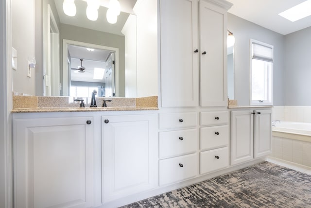 bathroom featuring vanity, tiled tub, a wealth of natural light, and a skylight