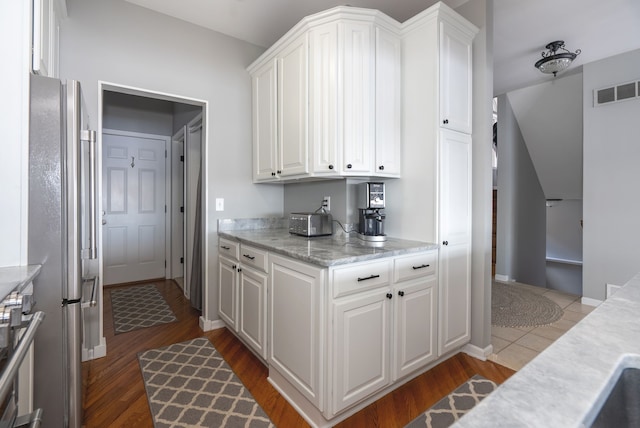 kitchen with wood-type flooring, stainless steel fridge, and white cabinets