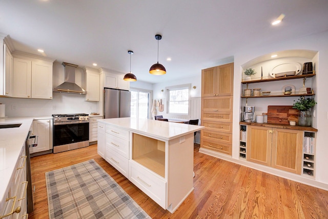 kitchen featuring appliances with stainless steel finishes, wall chimney exhaust hood, white cabinets, pendant lighting, and a center island