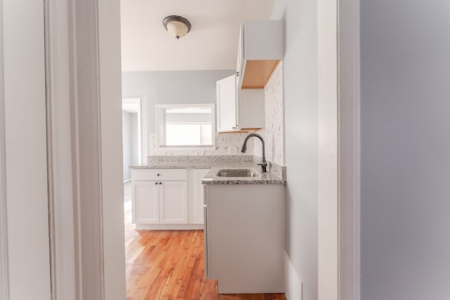 kitchen with white cabinetry, sink, light hardwood / wood-style flooring, and light stone countertops