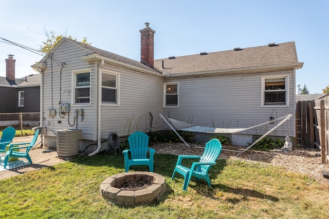 rear view of property with an outdoor fire pit, central air condition unit, fence, a lawn, and a chimney