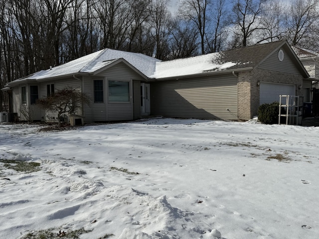 view of snowy exterior featuring a garage, brick siding, and central air condition unit