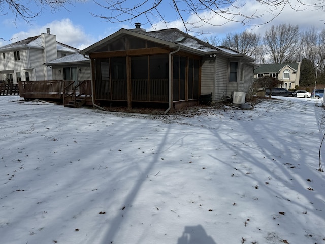 snow covered property featuring central air condition unit, a sunroom, and a deck