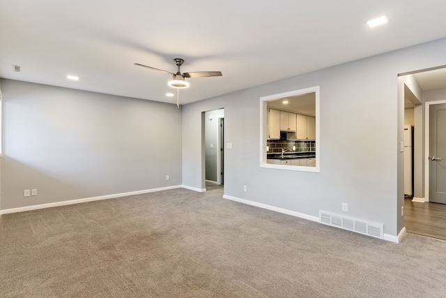 unfurnished room featuring sink, light colored carpet, and ceiling fan